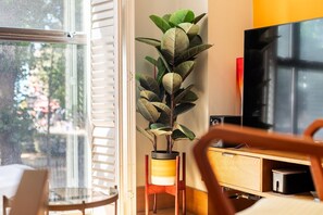 A room with a large window, a potted plant, a TV, and a wooden cabinet. - Stylish Angel & Islington Apartment (London)