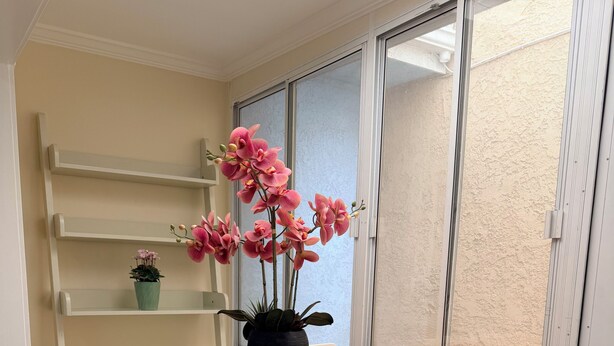 A dining area with a wooden table, white chairs, and a potted orchid plant. - Paradise at Sunset Shore 1-bedroom apartment with the Huntington Beach breeze (Huntington Beach)