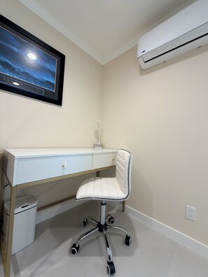 A white desk with a chair, a framed picture on the wall, and an air conditioner mounted on the wall. - Paradise at Sunset Shore 1-bedroom apartment with the Huntington Beach breeze (Huntington Beach)