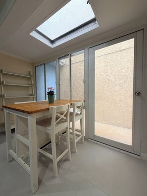 A room with a skylight, a sliding glass door, a wooden table, and white chairs. - Paradise at Sunset Shore 1-bedroom apartment with the Huntington Beach breeze (Huntington Beach)