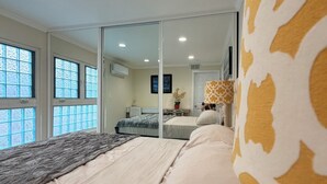 A bedroom with a bed, a mirror, and a window. - Paradise at Sunset Shore 1-bedroom apartment with the Huntington Beach breeze (Huntington Beach)