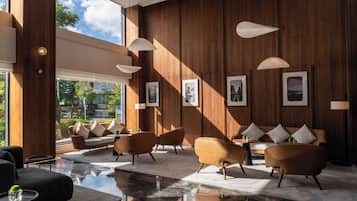 A modern lobby with wooden paneling, a marble floor, and a seating area with sofas and armchairs.