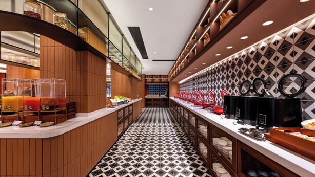 A modern hotel lobby with a central serving area, wooden paneling, and a patterned floor. - Intercity Hotel Lijiang Dashuiche (Lijiang)