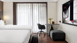 Hotelkamer met twee bedden, een bureau, een stoel, een tafeltje met een bloemenvaas en een grote spiegel.