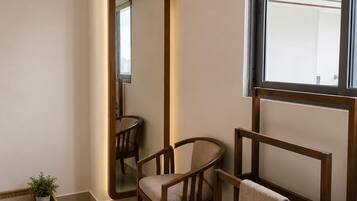 A modern bedroom with a large mirror, two wooden chairs, a bed, and a small potted plant.