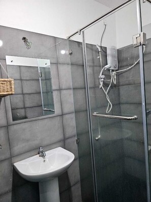 A bathroom with a glass-enclosed shower, a white sink, and a mirror.