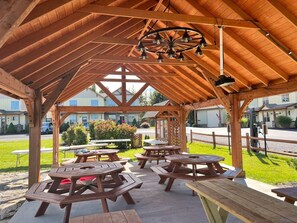 A covered outdoor area with picnic tables and a wooden ceiling structure. - BBC 12 Hot Tub Fireplace Near Lift and Slope (Snowshoe)