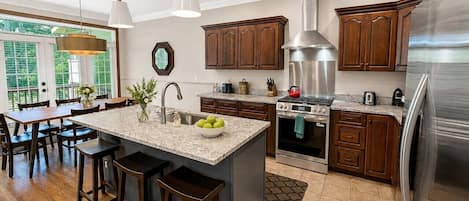 A modern kitchen with a central island, wooden cabinets, stainless steel appliances, and a dining area with bar stools.