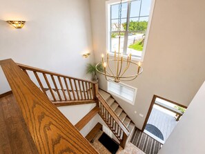 A wooden staircase with a chandelier, a window with a view, and a plant. - BBC 12 Snowshoe Ski in out 5BR Home Near Slopes (Snowshoe)