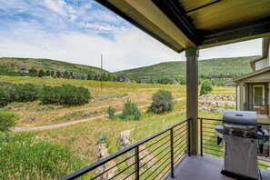 Ein Balkon mit Grill, mit Blick auf eine grüne Landschaft und Häuser in der Ferne.