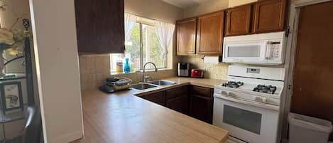 A kitchen with wooden cabinets, a white stove, a microwave, and a sink.