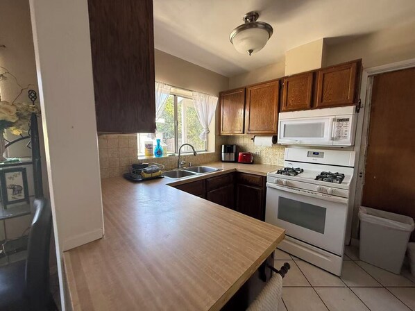 A kitchen with wooden cabinets, a white stove, a microwave, and a sink. - Beautiful 3-bedroom house with big yard (Duarte)