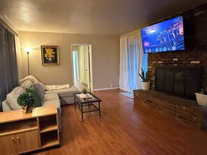 A living room with a sofa, a coffee table, a TV mounted on the wall, and a fireplace. - Beautiful 3-bedroom house with big yard (Duarte)