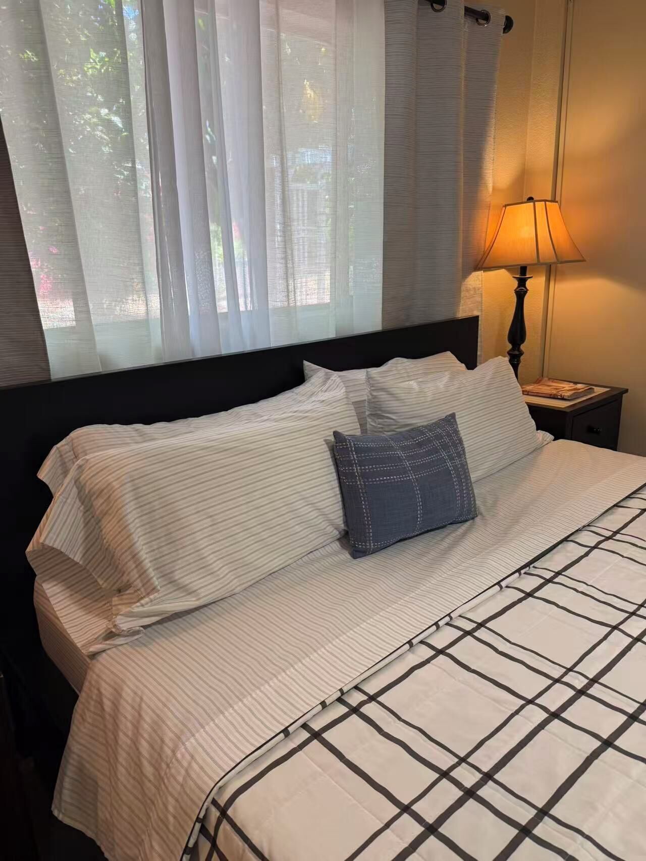 A neatly made bed with striped bedding, a pillow, and a lamp on a bedside table.