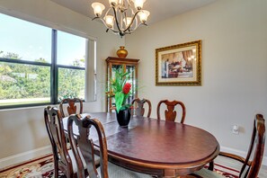 A dining room with a round wooden table, six chairs, a chandelier, a vase with flowers, a cabinet, and a framed picture on the wall. - 6 Mi to Port Charlotte Beach Park! Family Getaway (Port Charlotte)