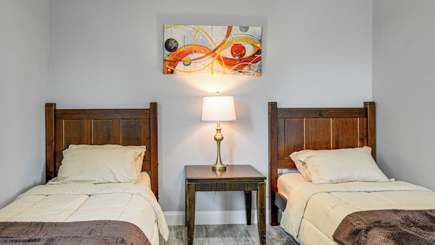 Een hotelkamer met twee éénpersoonsbedden, een klein nachtkastje met een lamp, en een kleurrijk abstract schilderij aan de muur.