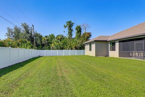 A backyard with a white fence, a grassy lawn, and a building with a garage. - 6 Mi to Port Charlotte Beach Park! Family Getaway (Port Charlotte)
