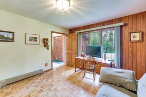 A room with a wooden floor, a desk with a chair, a television, and a window with a view of trees. - Private Beach on Lake Huron! Group Retreat w/ Deck (Cheboygan)