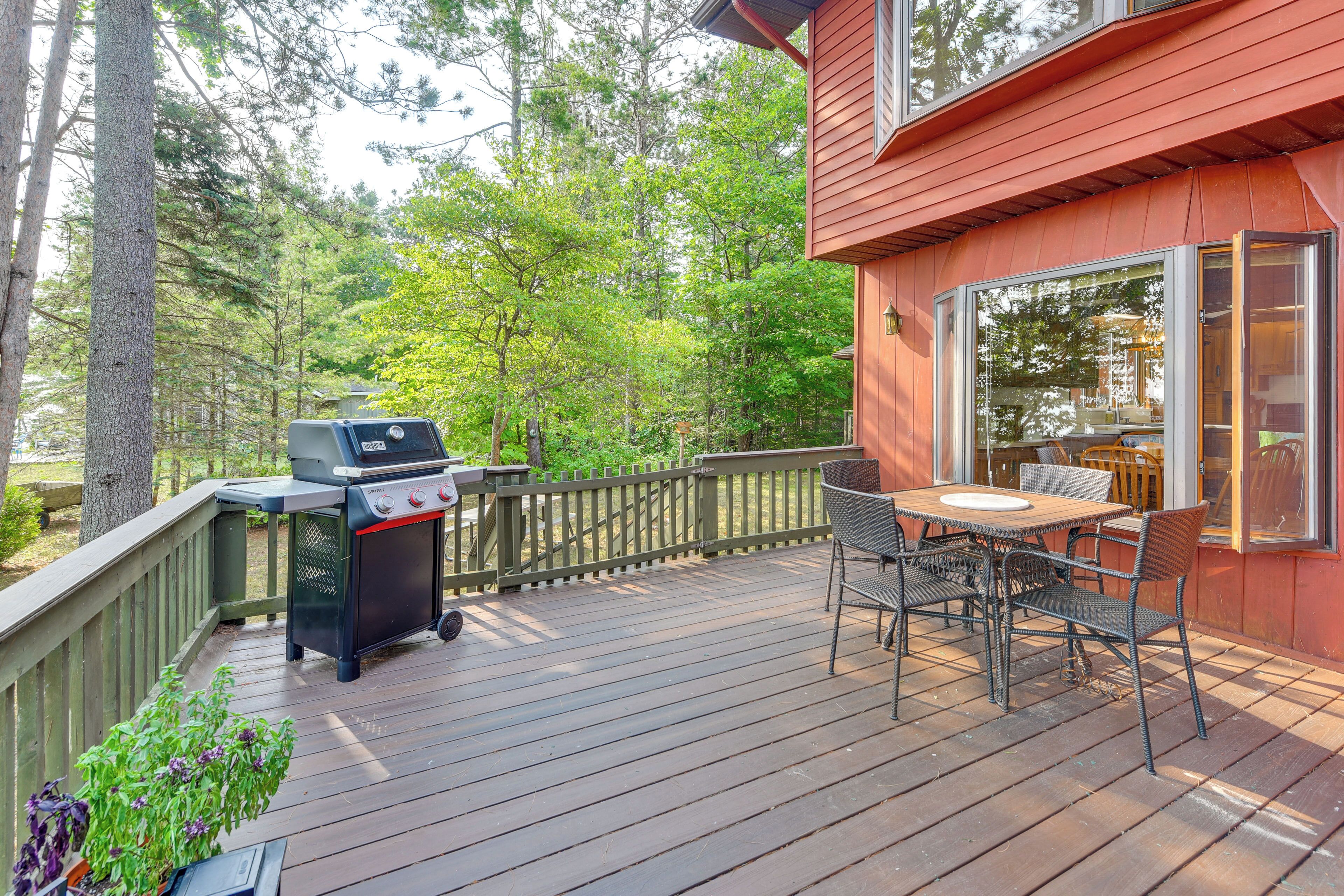Een terras met een barbecue, tuinmeubilair en uitzicht op het omliggende bos.