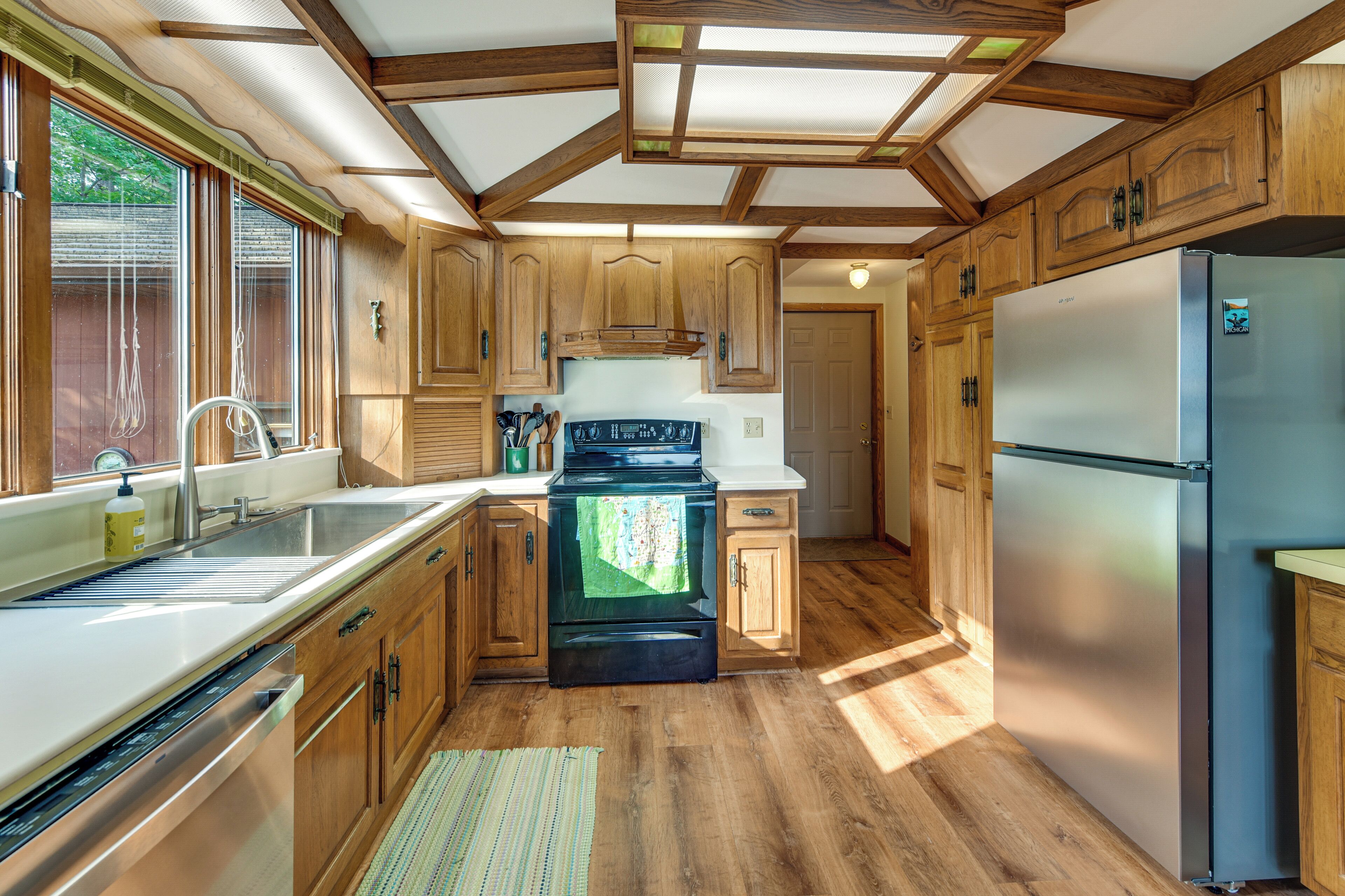 Une cuisine avec des meubles en bois, un réfrigérateur en acier inoxydable, une cuisinière et une fenêtre avec des stores.