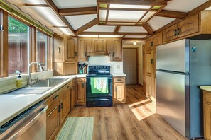 A kitchen with wooden cabinets, a stainless steel refrigerator, a stove, and a window with blinds. - Private Beach on Lake Huron! Group Retreat w/ Deck (Cheboygan)