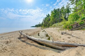 A sandy beach with a fallen tree, a wooden staircase, and a forest in the background. - Private Beach on Lake Huron! Group Retreat w/ Deck (Cheboygan)