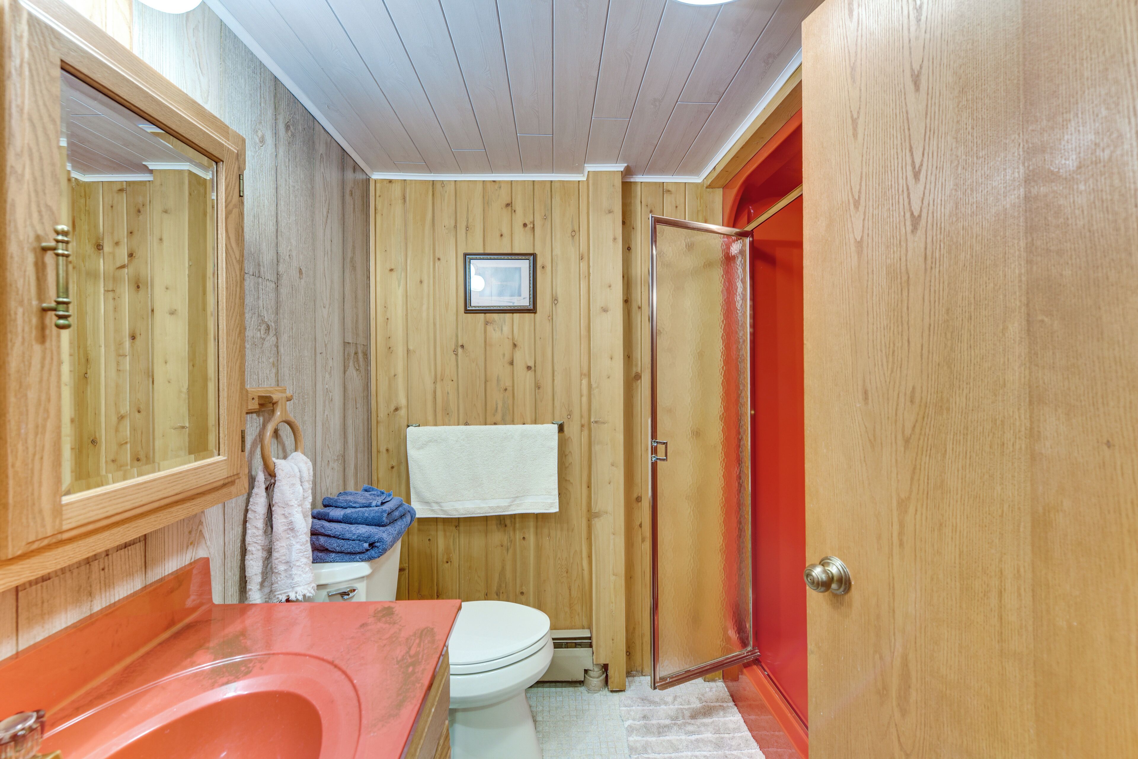 Ein Badezimmer mit Holzverkleidung, einer weißen Toilette, einer roten Badewanne und einem Handtuchhalter mit gefalteten Handtüchern.