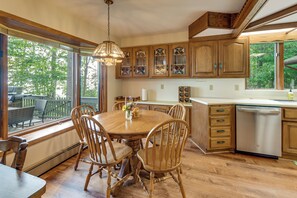 A kitchen with wooden cabinets, a dining table with chairs, and a view of the outdoors through large windows. - Private Beach on Lake Huron! Group Retreat w/ Deck (Cheboygan)