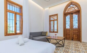 A room with a bed, a sofa, a small table, and two windows with wooden frames.