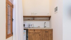 Een kleine keuken met houten kastjes, een magnetron, een waterkoker en een spoelbak.