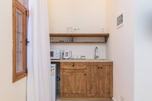 A compact kitchen with wooden cabinets, a microwave, a kettle, and a sink.