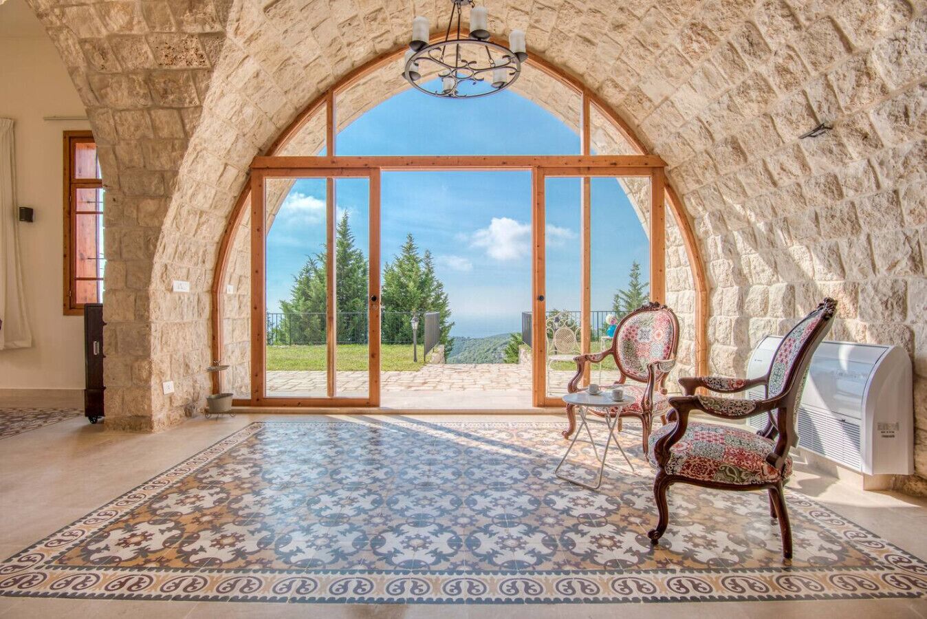 Ein Zimmer mit einem steinernen Bogen, der auf einen Balkon mit Blick auf Bäume und den Himmel führt.