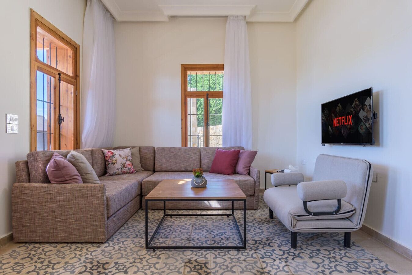 Una sala de estar con un sofá modular, una mesa de centro, una silla y un televisor montado en la pared.