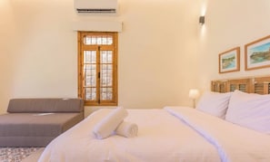 A hotel room with a bed, a sofa, a window with a view, and a wall-mounted air conditioner.