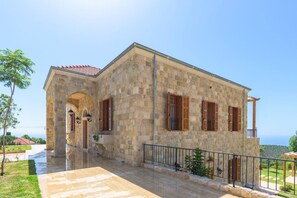 A stone building with a red-tiled roof, a covered entrance, and a balcony with a metal railing.