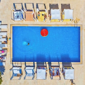 An aerial view of a swimming pool with multiple sun loungers and a red circular object in the center.