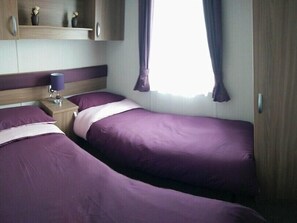 Ein Schlafzimmer mit zwei Betten, einem Nachttisch mit Lampe und einem Fenster mit Vorhängen.
