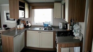 A compact kitchen with a sink, cabinets, and a window. - Hafan y Mor Haven - Holiday Accommodation 7021 (Pwllheli)