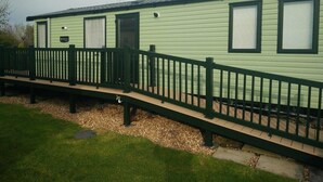 A single-story mobile home with a green exterior, a covered porch, and a small deck. - Hafan y Mor Haven - Holiday Accommodation 7021 (Pwllheli)