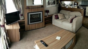 A modern living room with a sofa, a coffee table, a fireplace, and a television. - Hafan y Mor Haven - Holiday Accommodation 7021 (Pwllheli)