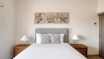 A neatly made bed with patterned pillows, two bedside tables with lamps, and three wall-mounted artwork pieces depicting shells and a starfish.