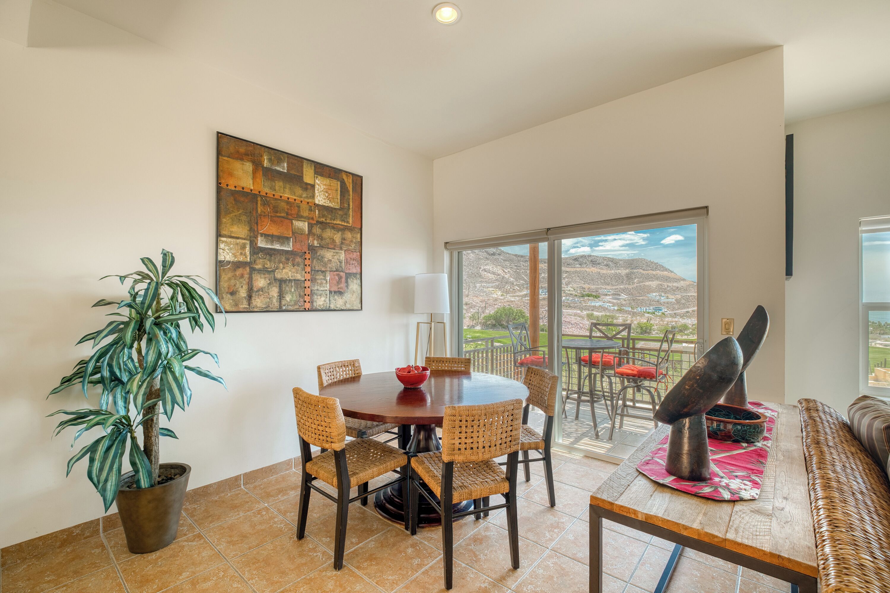 A dining area with a round table, wicker chairs, a potted plant, and a view of the outdoors.