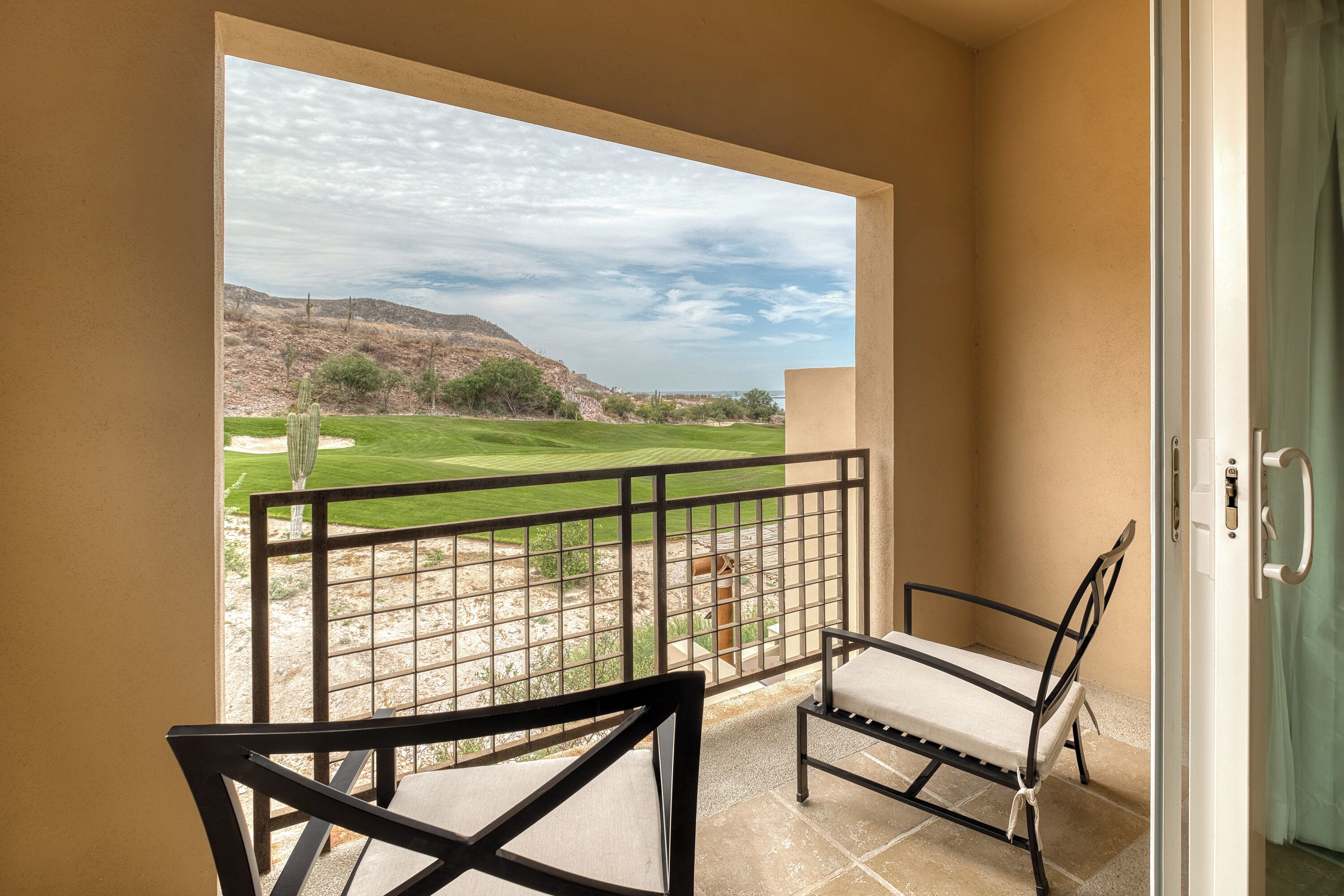 A balcony with two chairs, a view of a golf course, and a door leading to a room.
