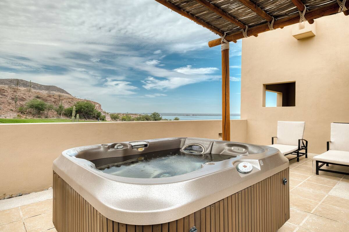 A hot tub on a balcony with a view of the sea and a desert landscape.