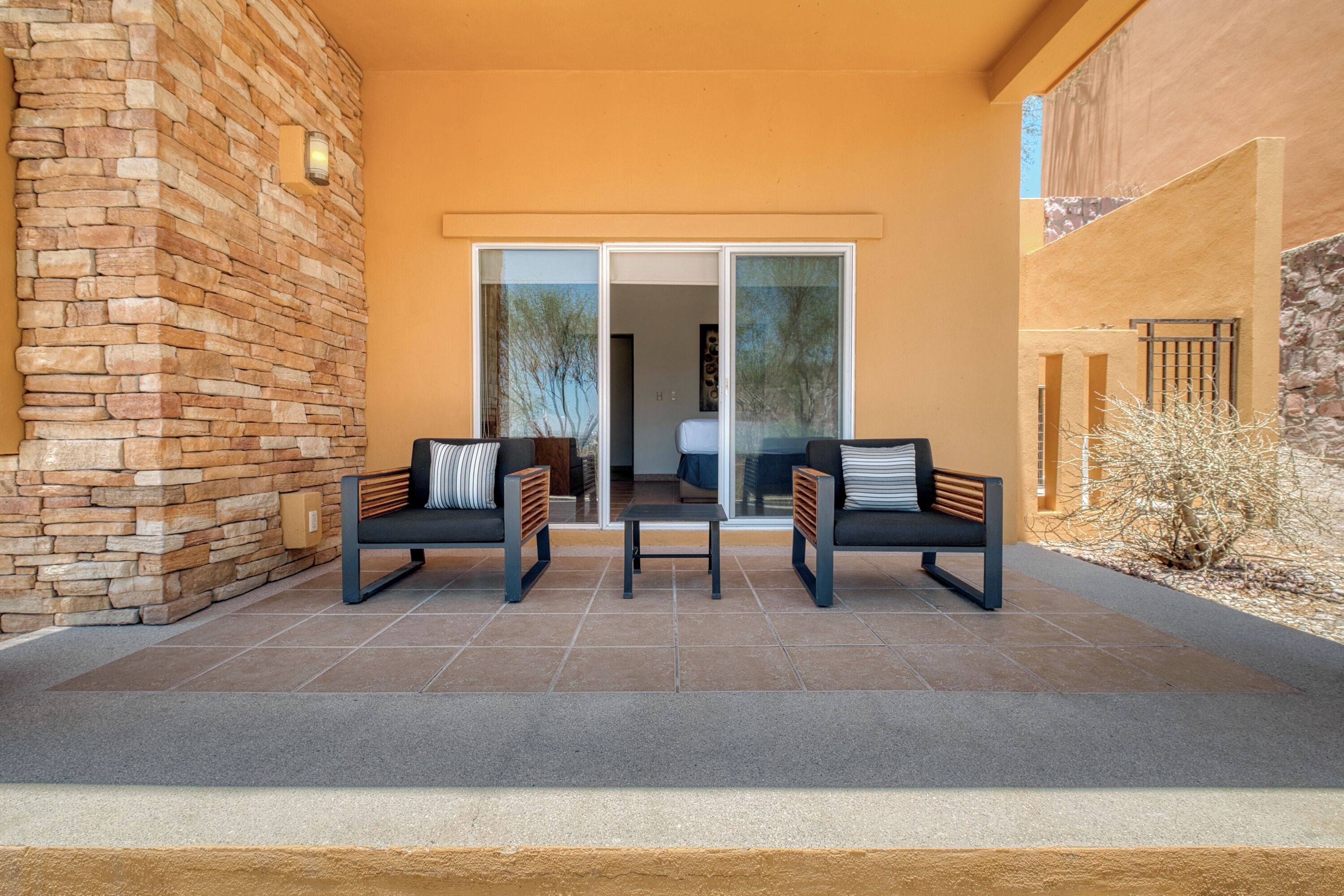 A patio with two chairs and a table, a stone wall, and a sliding glass door leading to an interior space.
