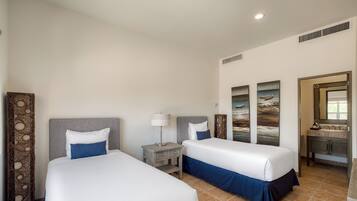 Habitación de hotel con dos camas, una mesita de noche, una lámpara y baño con lavabo y espejo.