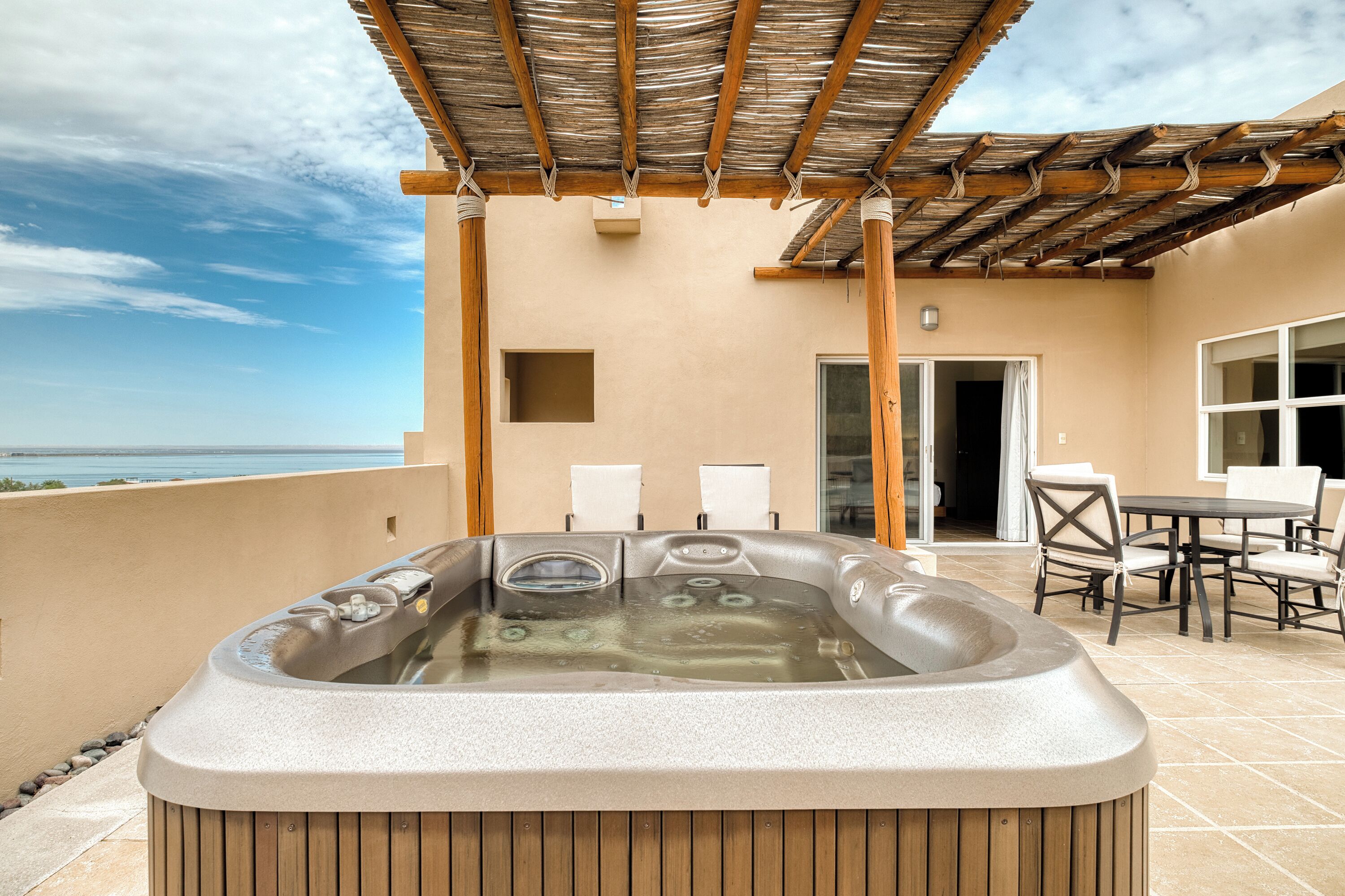 Un jacuzzi sur un balcon avec vue sur la mer, un espace salon couvert et une porte donnant sur un espace intérieur.