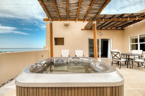 Un jacuzzi en un balcón con vistas al mar, un área de estar techada y una puerta que da a un espacio interior.