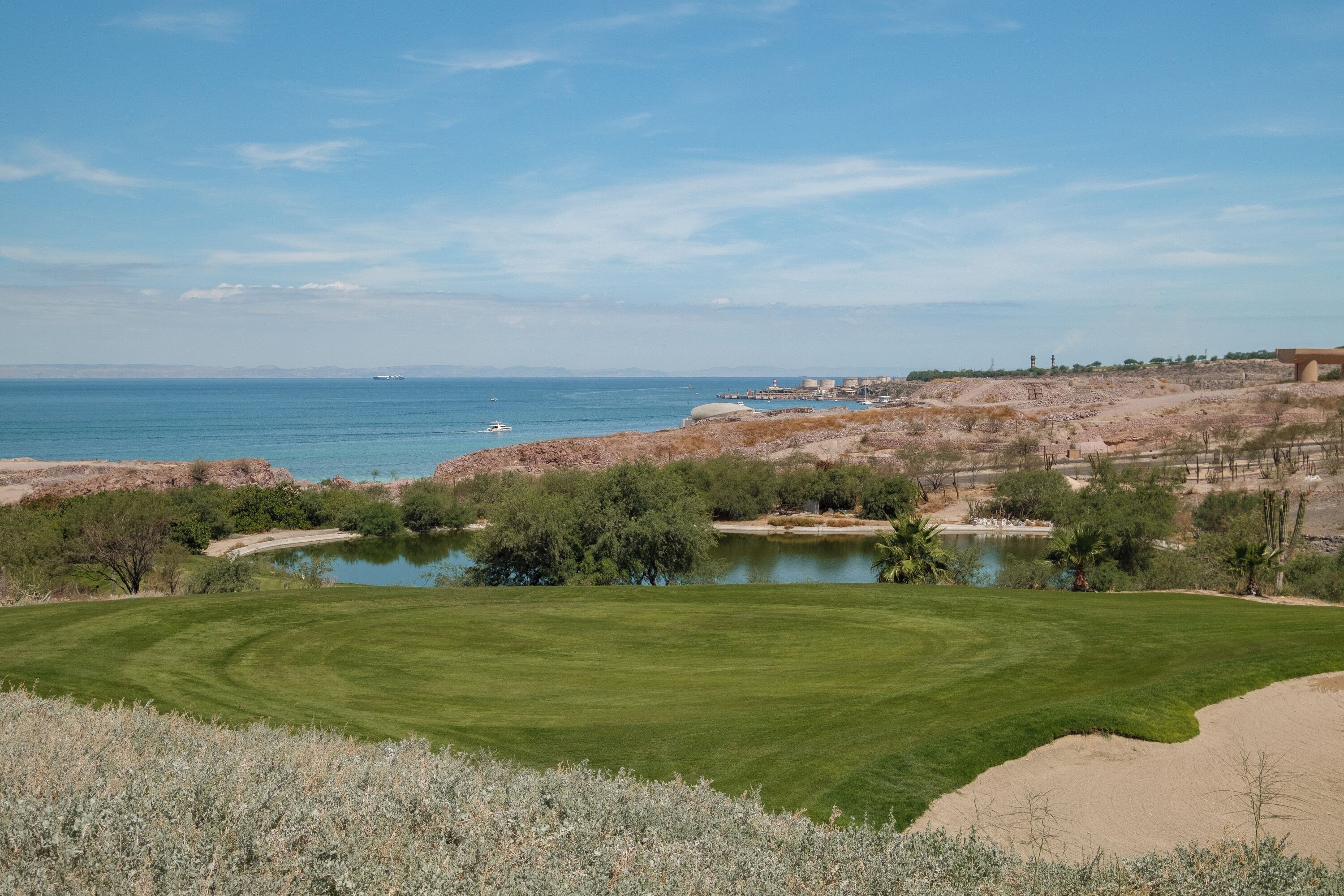 Un campo de golf con un estanque, una zona arenosa y vistas al mar.