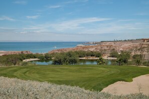 Un campo de golf con un estanque, una zona arenosa y vistas al mar.